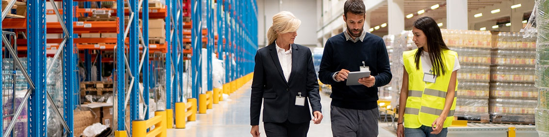 three warehouse workers walking through the inventory floor reviewing metrics on a wms