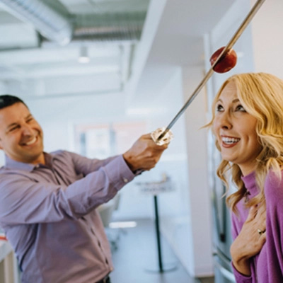 Man cutting an apple over coworker's head