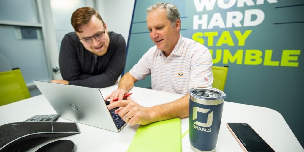 two male collegues smiling and discussing a project on a laptop