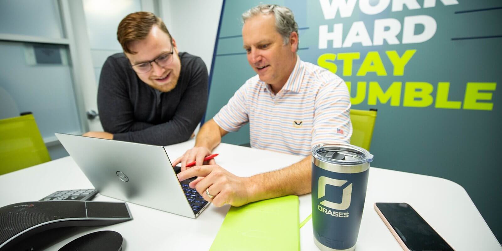 two male collegues smiling and discussing a project on a laptop