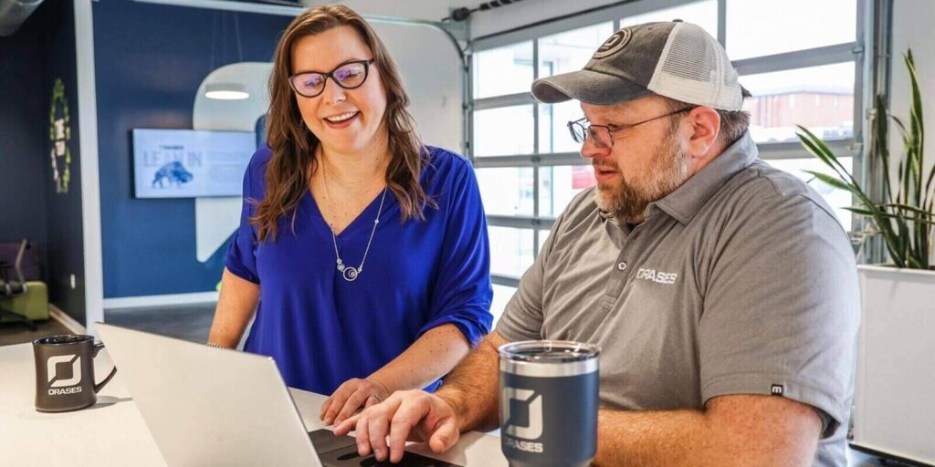 two office collegues smiling and discussing a project on laptop
