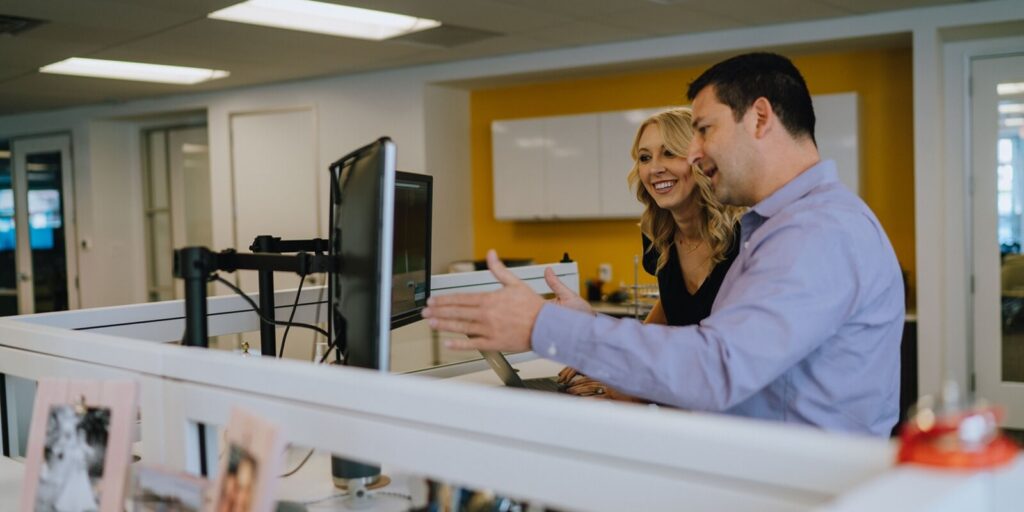 colleagues collaborating at a workstation in a modern office space, discussing content on a computer monitor