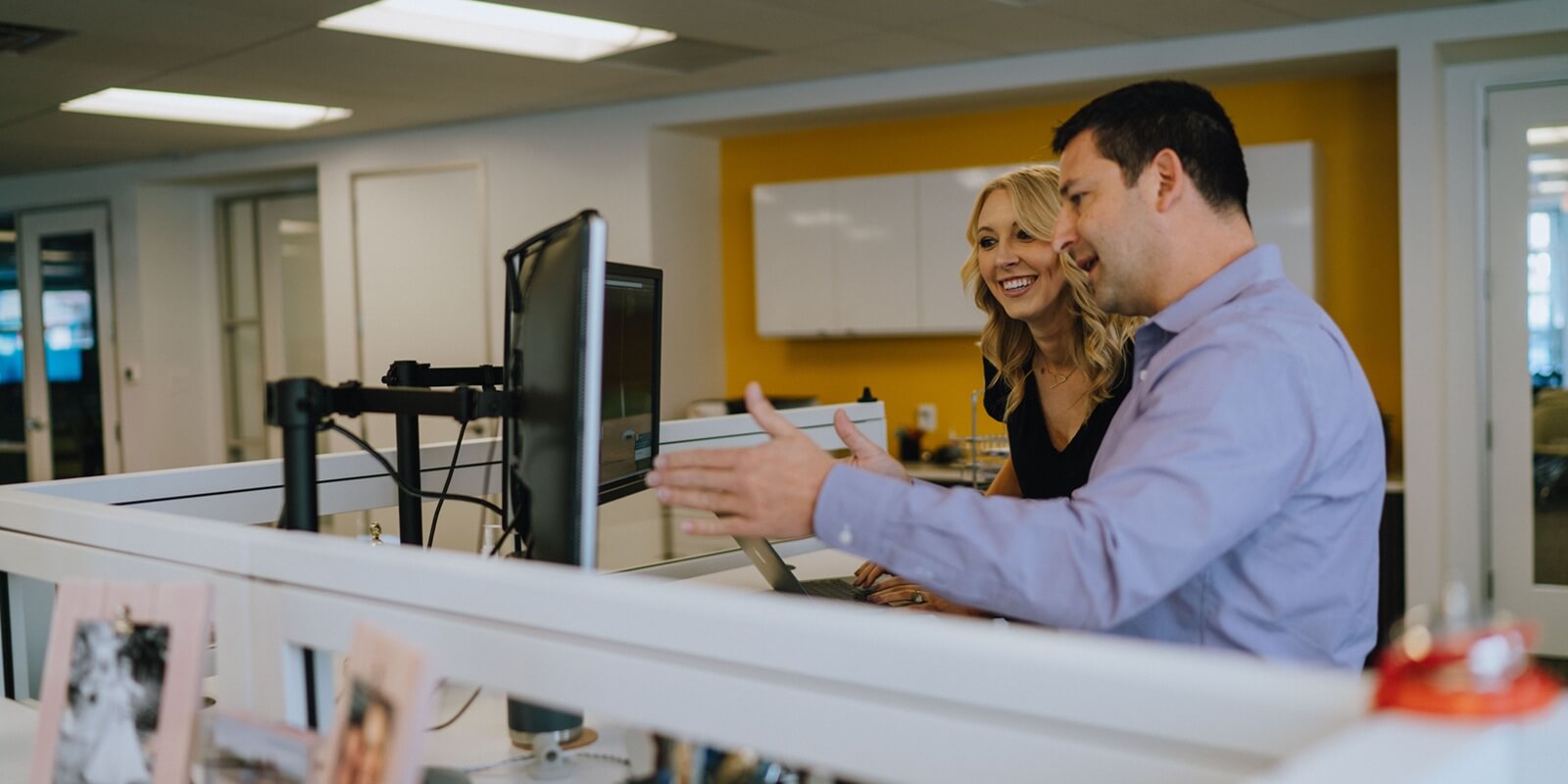 colleagues collaborating at a workstation in a modern office space, discussing content on a computer monitor
